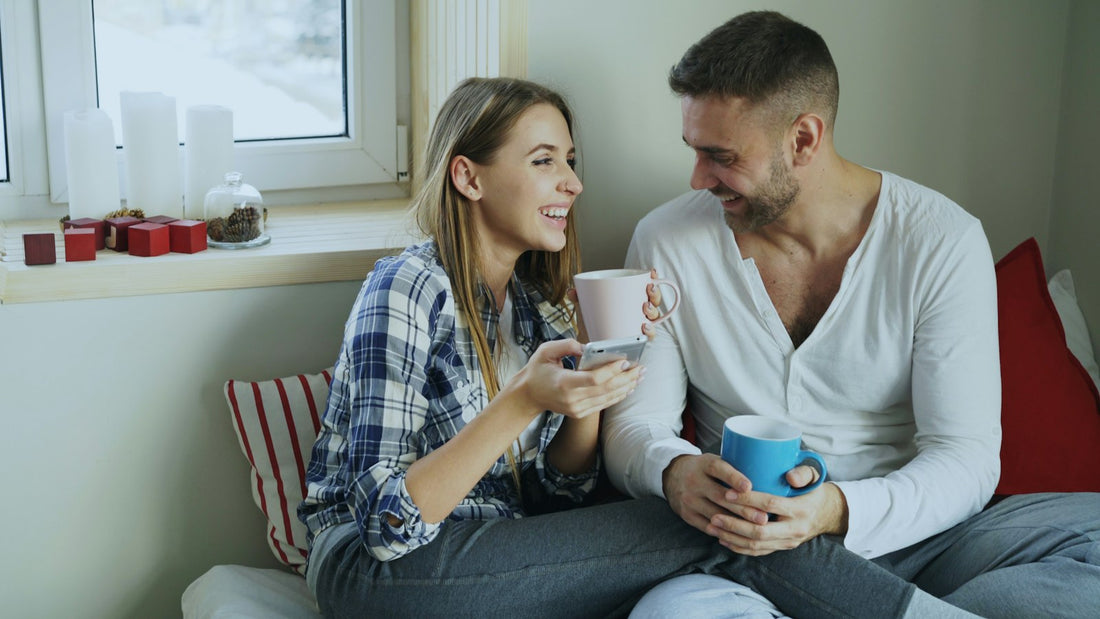 Una pareja conversa y se ríe mientras toma café en el sofá